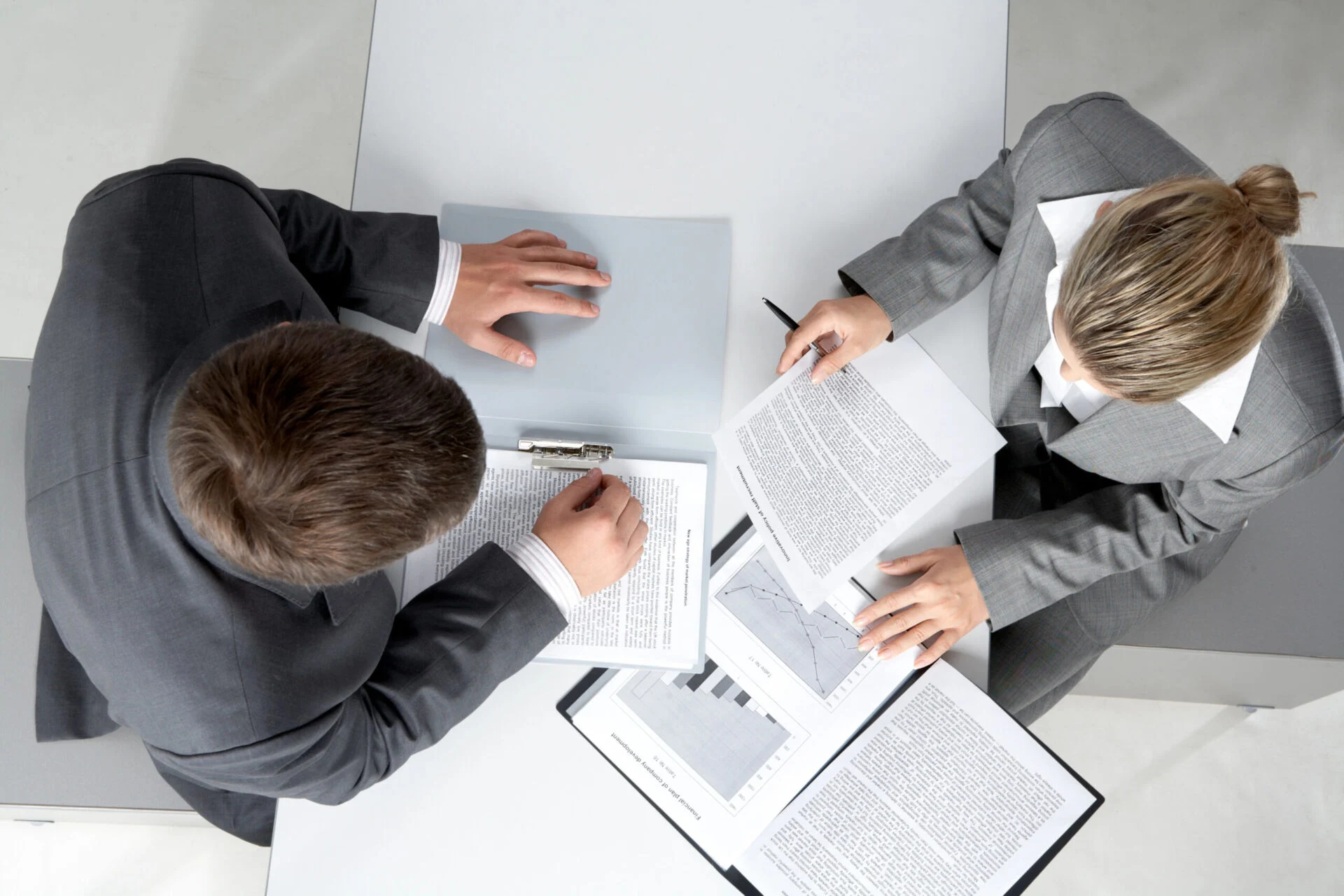 Two people share a desk while looking at papers and charts