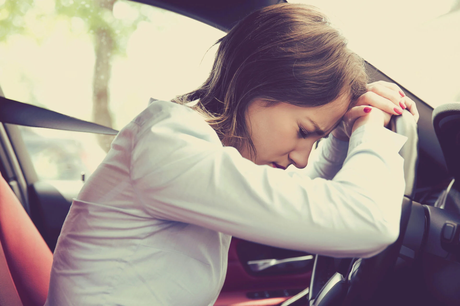 Distraught woman lays her head on her steering wheel of the vehicle