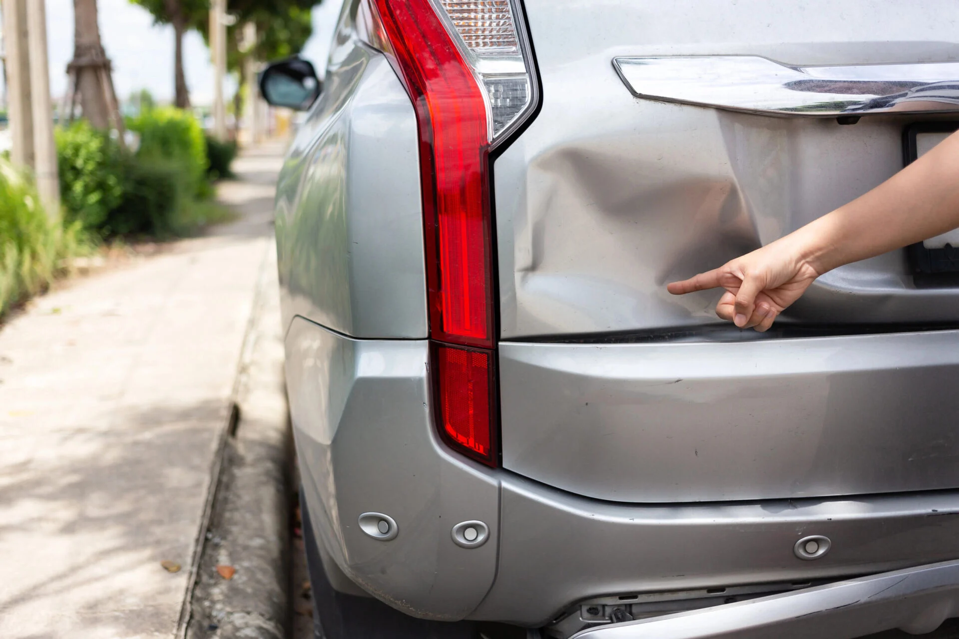 Person pointing to dent on the back of silver car