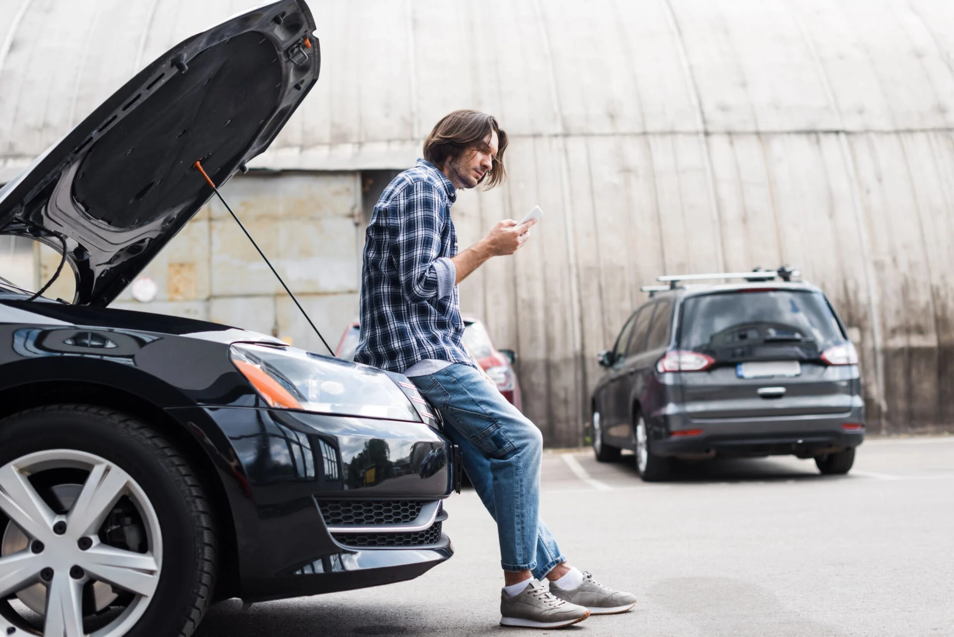 Man standing near broken vehicle with phone in hand.
