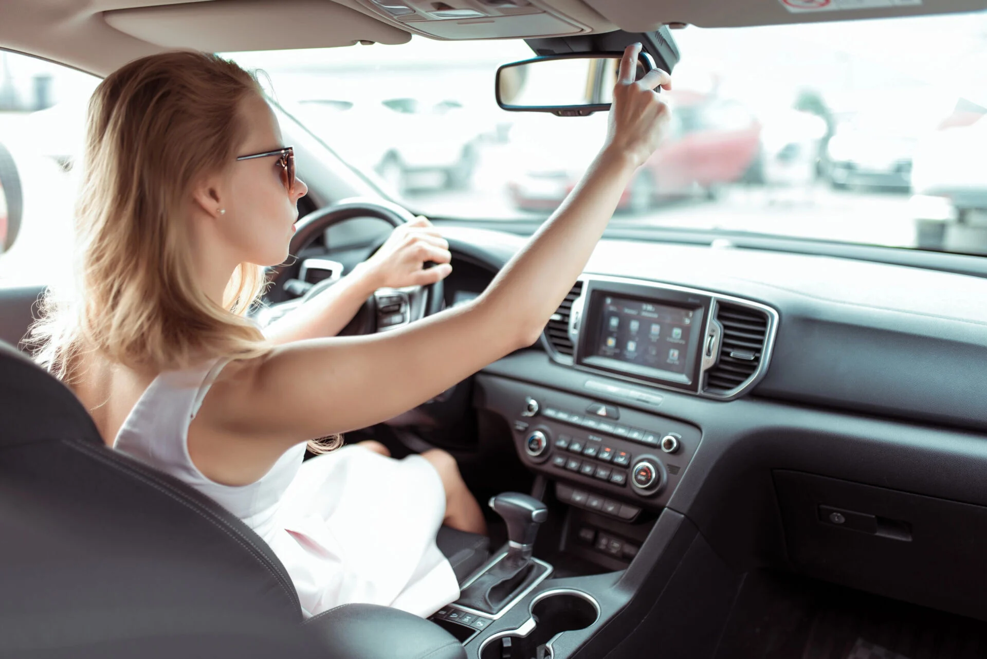 Woman adjusting rearview mirror while sitting in the drivers seat.