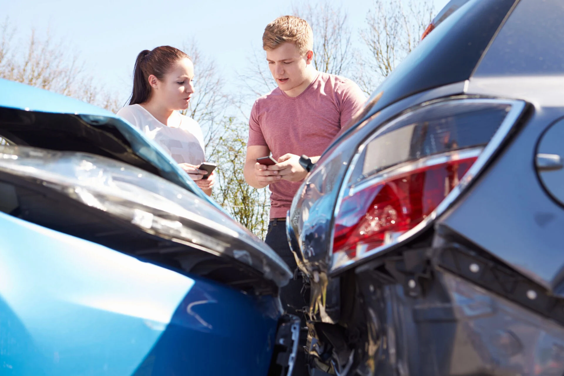 Man and woman exchange information on their cell phones after one car rear ends another