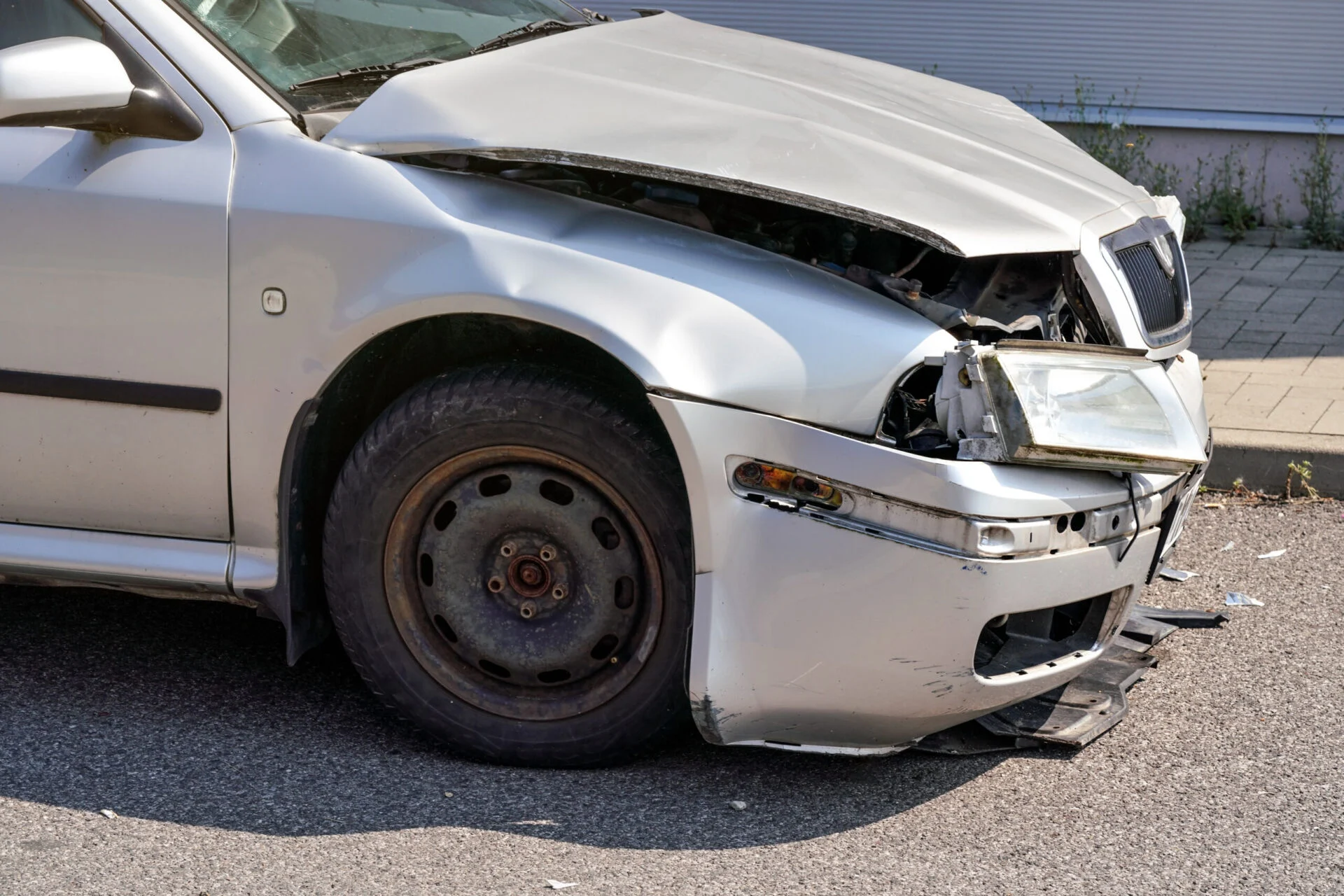 Silver car with its front crashed, plates dented and broken on road.