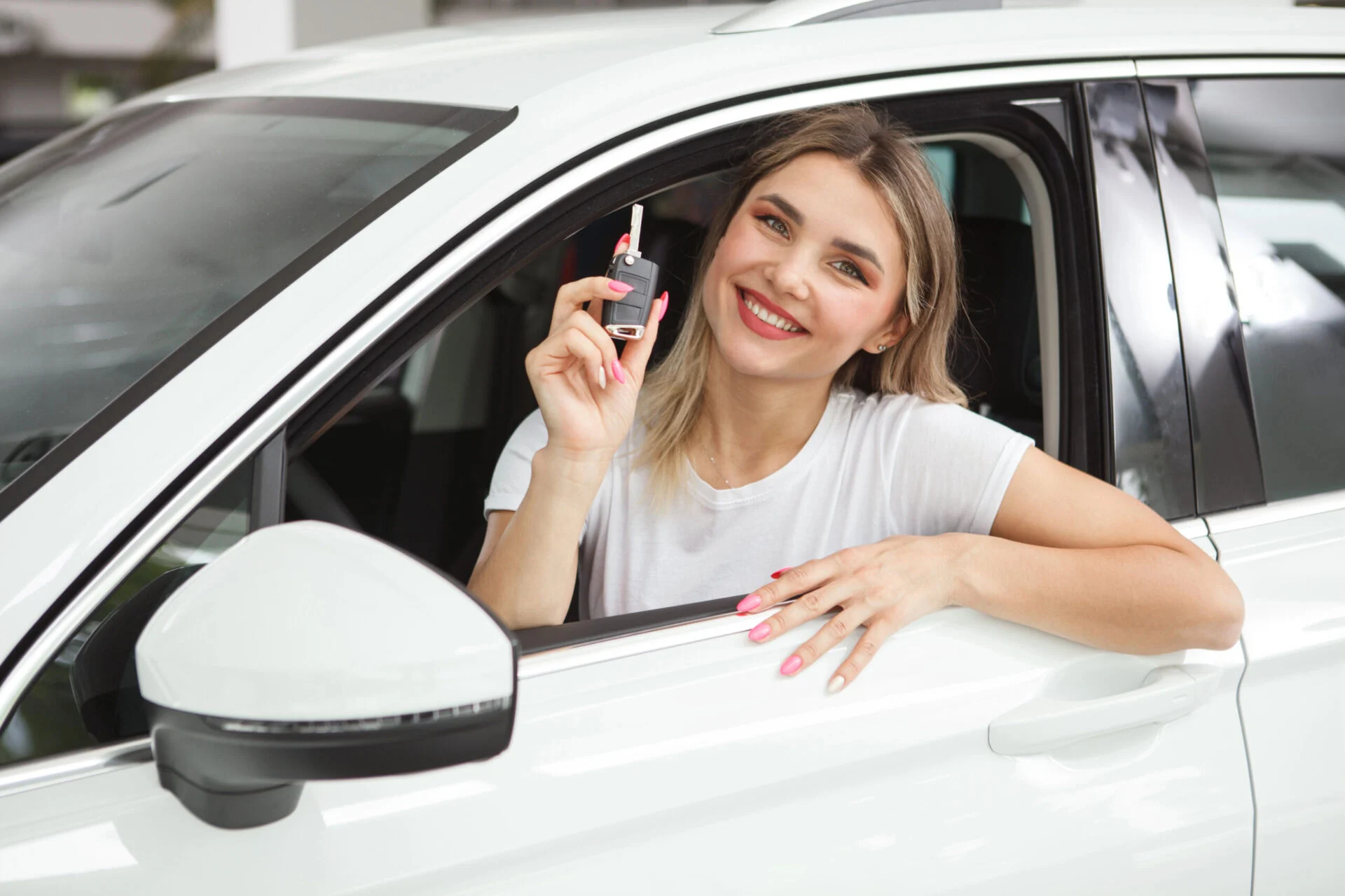 Young female driver sitting inside drivers seat showing car keys.