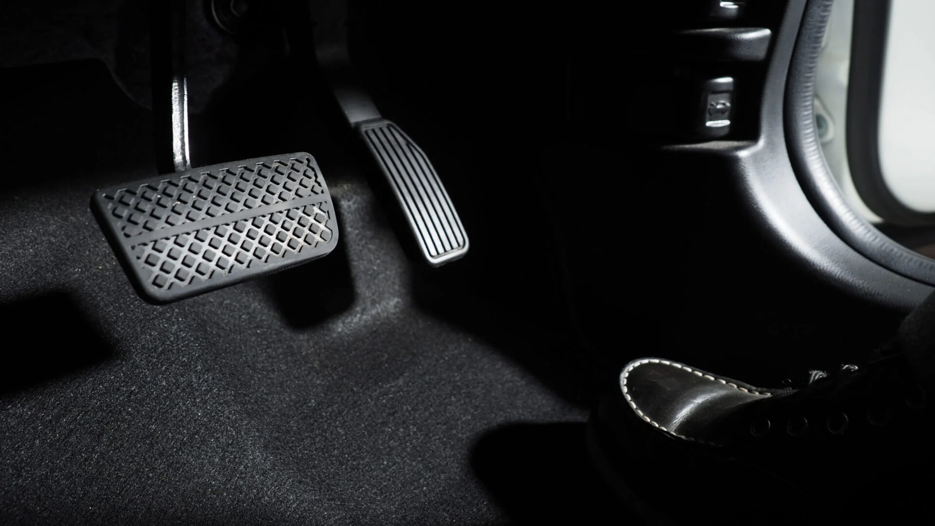 Floor of a vehicle with a driver's foot. Both break and gas pedals visible.
