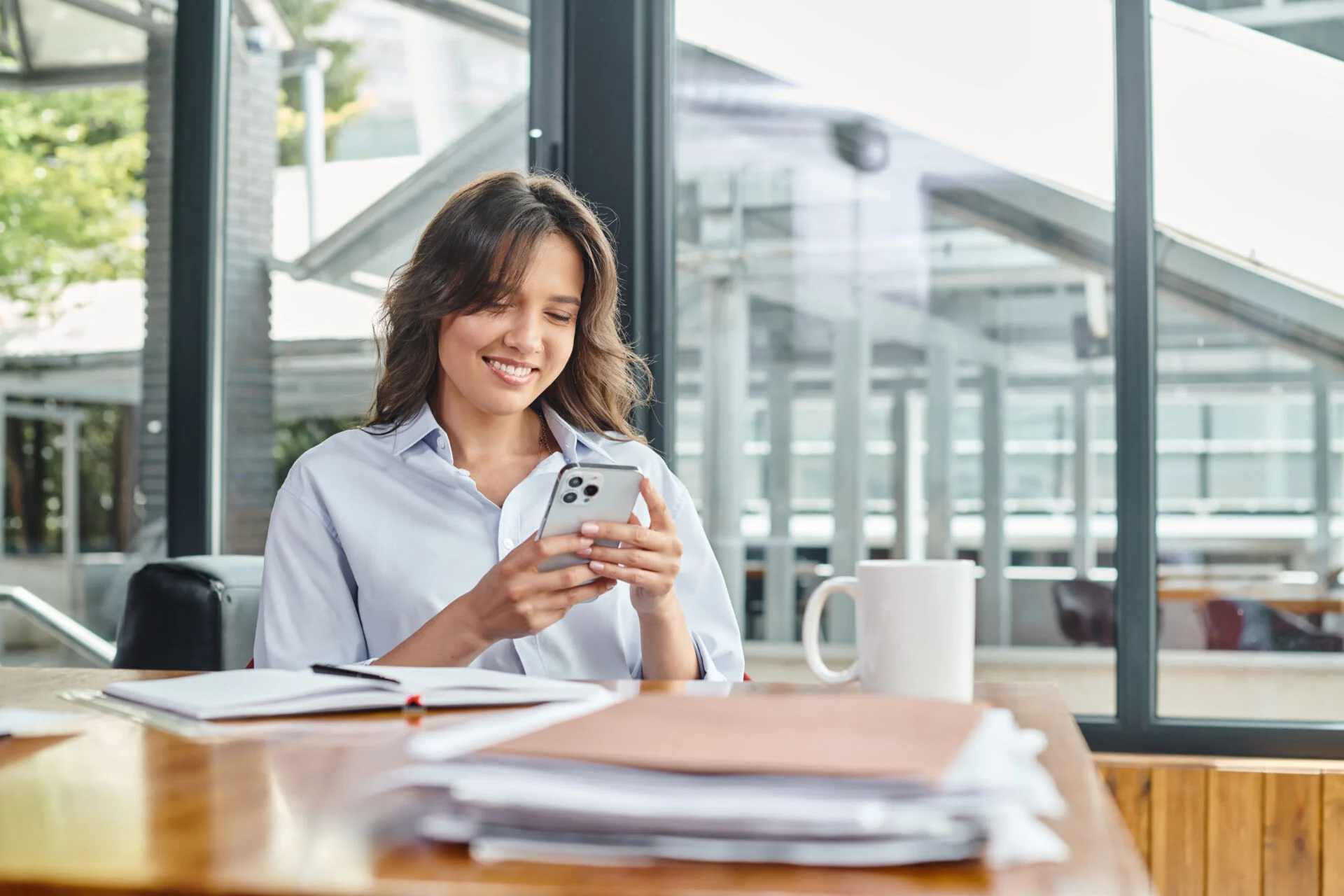 Woman sits at a desk looking at her phone with a smile