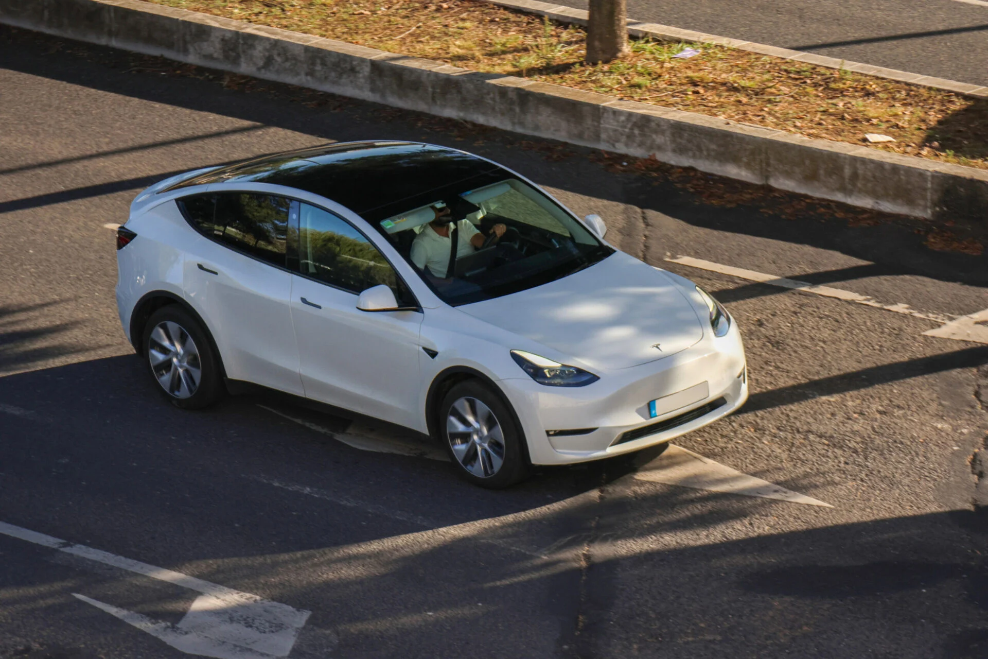 White Tesla Model Y driving on a sunny street.